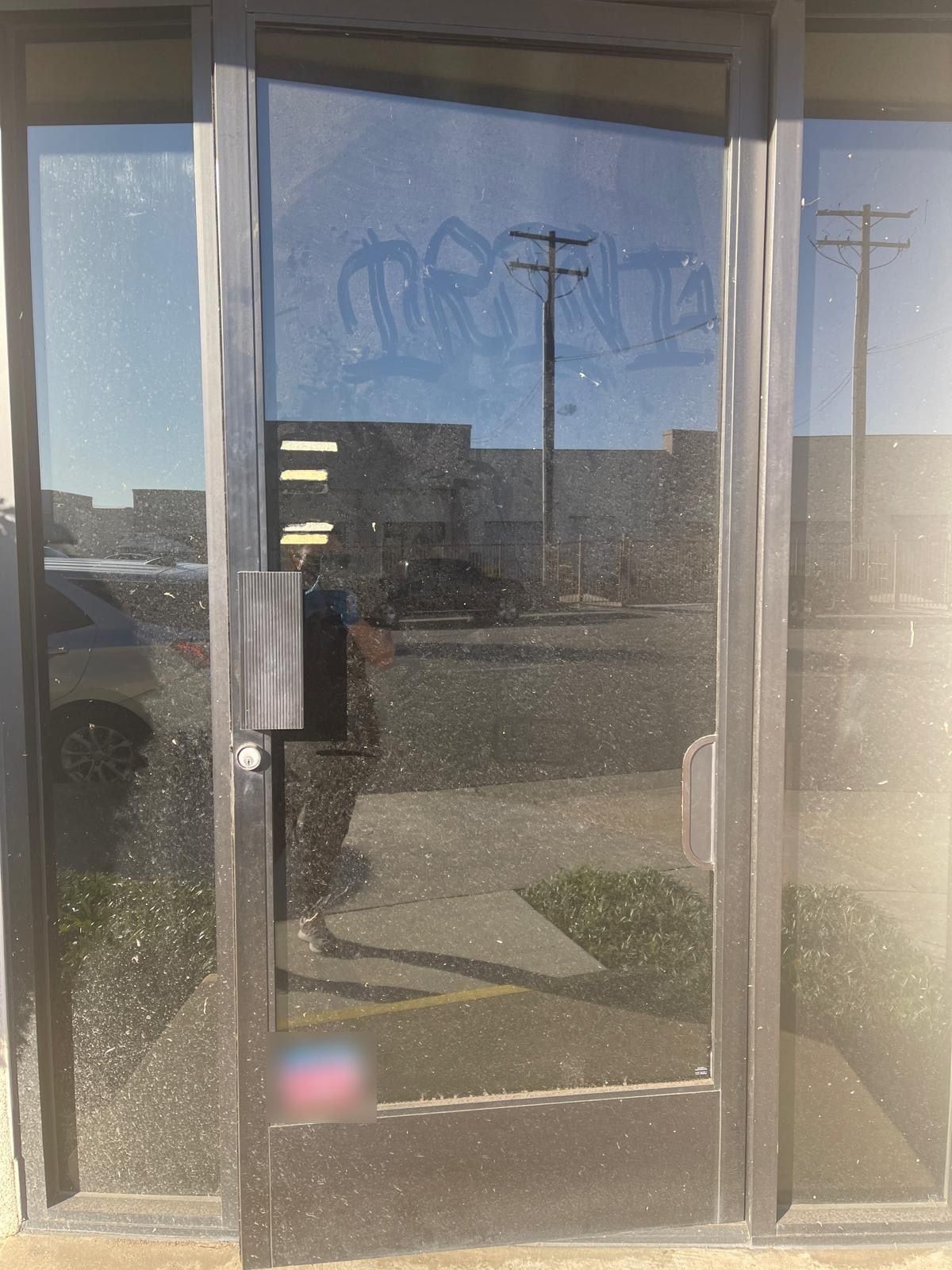 A glass entry door coated in dust, with writing traced in the dirt