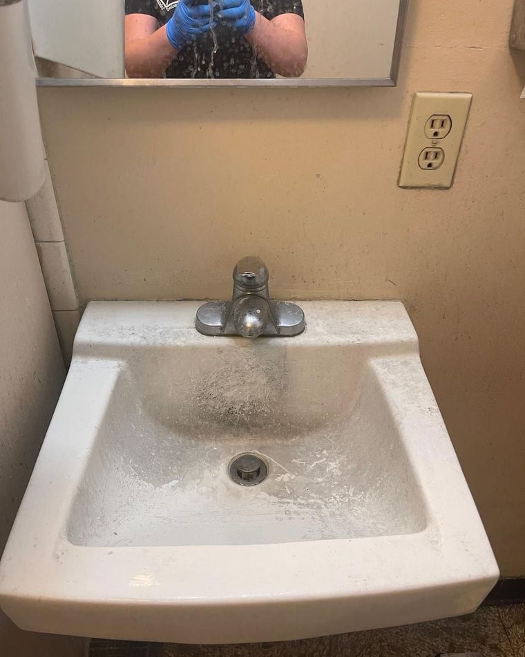 A restroom sink covered in cleaning powder, with gloved hands reflected in the mirror