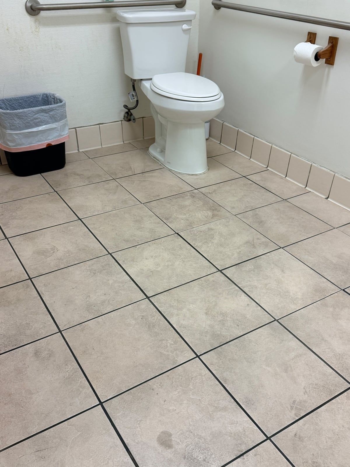 A restroom tile floor with footprints, dull patches, and a dark spot