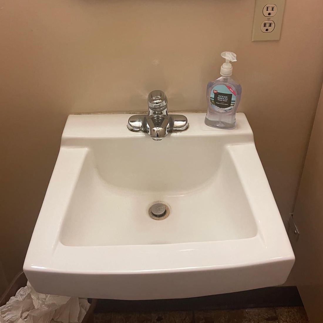 A clean wall-mounted restroom sink with a polished tap and a bottle of hand soap