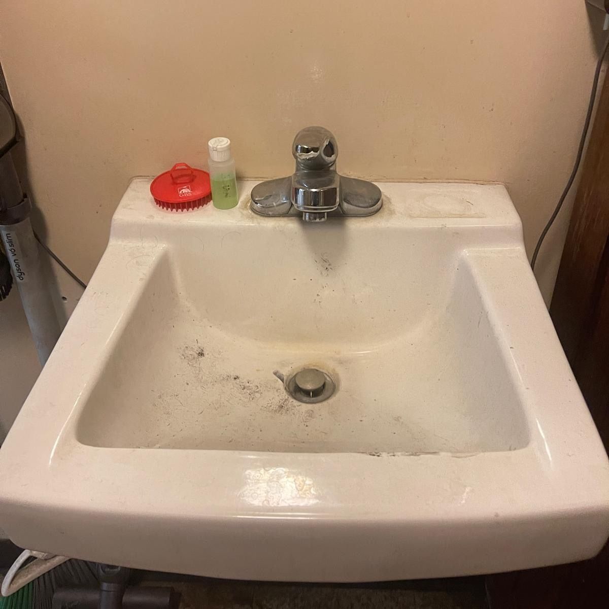 A wall-mounted restroom sink with dark grime around the drain and tap